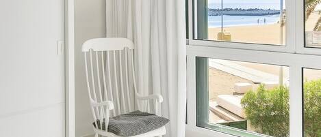 Una habitación con un ventanal grande, una mecedora y vista a la playa.
