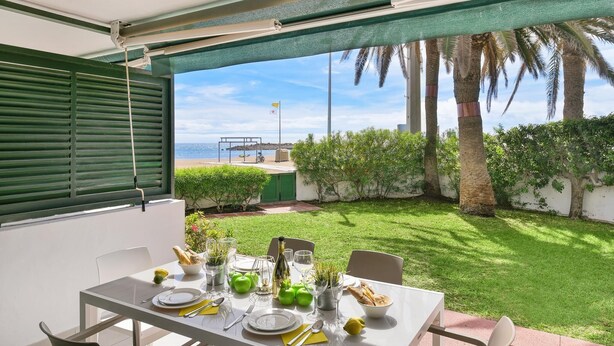 A dining area with a table set for two, overlooking a well-maintained garden and a view of the sea. - Beachfront Las Burras MRA 02 by VillaGranCanaria (San Bartolomé de Tirajana)