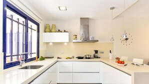 A modern kitchen with white cabinets, a stainless steel sink, and a window with blue frames. - Meloneras Bahia 7 by VillaGranCanaria (Maspalomas)