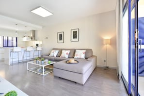 A modern living room with a grey sofa, a glass coffee table, and a kitchen area in the background. - Meloneras Bahia 7 by VillaGranCanaria (Maspalomas)
