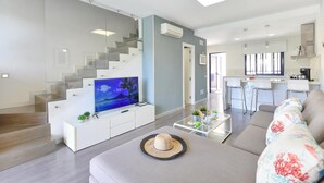 A modern living room with a flat-screen TV, a sofa, a coffee table, and a staircase leading to an upper floor. - Meloneras Bahia 7 by VillaGranCanaria (Maspalomas)