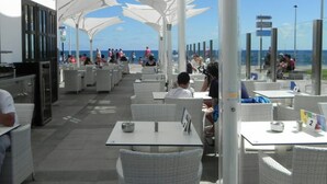 An outdoor dining area with white umbrellas, tables, and chairs, overlooking the sea. - Meloneras Bahia 7 by VillaGranCanaria (Maspalomas)