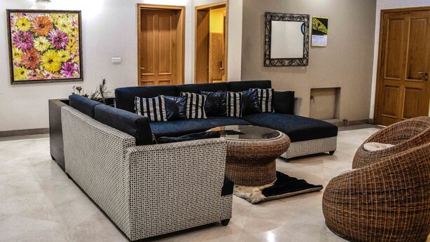 A living room with a sectional sofa, a round coffee table, and two wicker chairs. - Lahore Home Stay (Lahore)