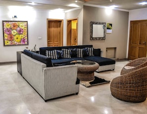 A living room with a sectional sofa, a round coffee table, and two wicker chairs. - Lahore Home Stay (Lahore)