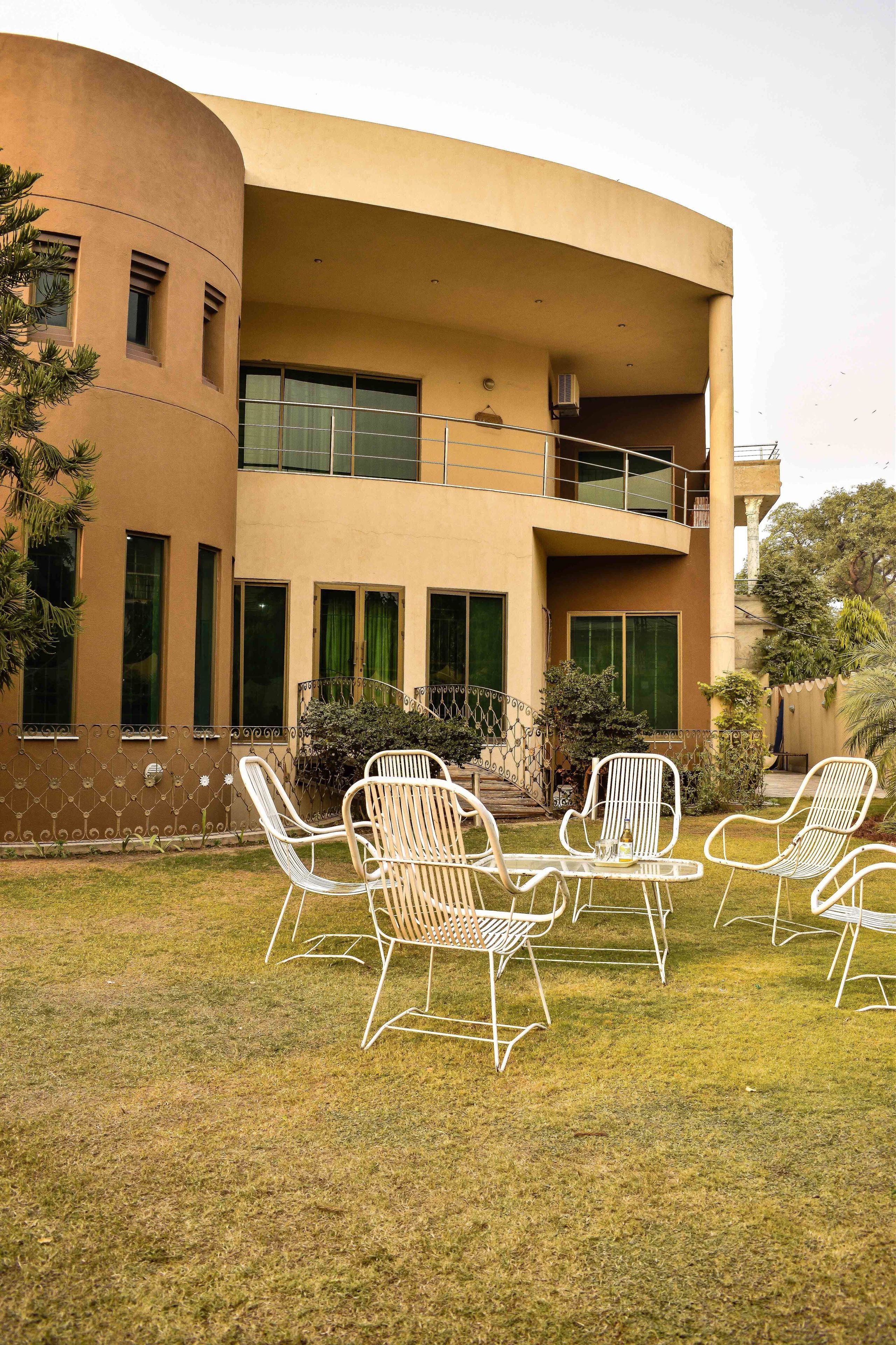 A two-story building with a curved facade, outdoor seating area with metal chairs, and a small balcony.