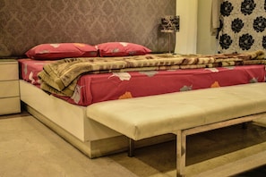 A bed with a red and beige bedspread, a bench, and a nightstand with a lamp. - Lahore Home Stay (Lahore)