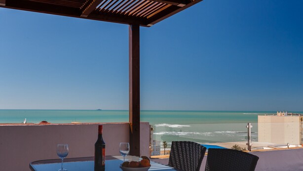 Ein Tisch mit einer Weinflasche und Gläsern, einer Obstschale und Blick auf den Ozean und Strand.
