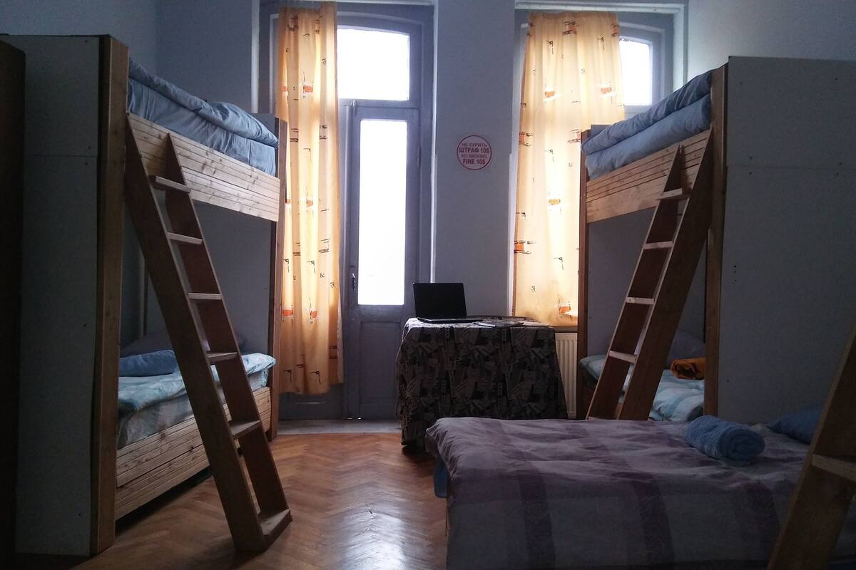 A dormitory room with bunk beds, a small table, and a laptop.