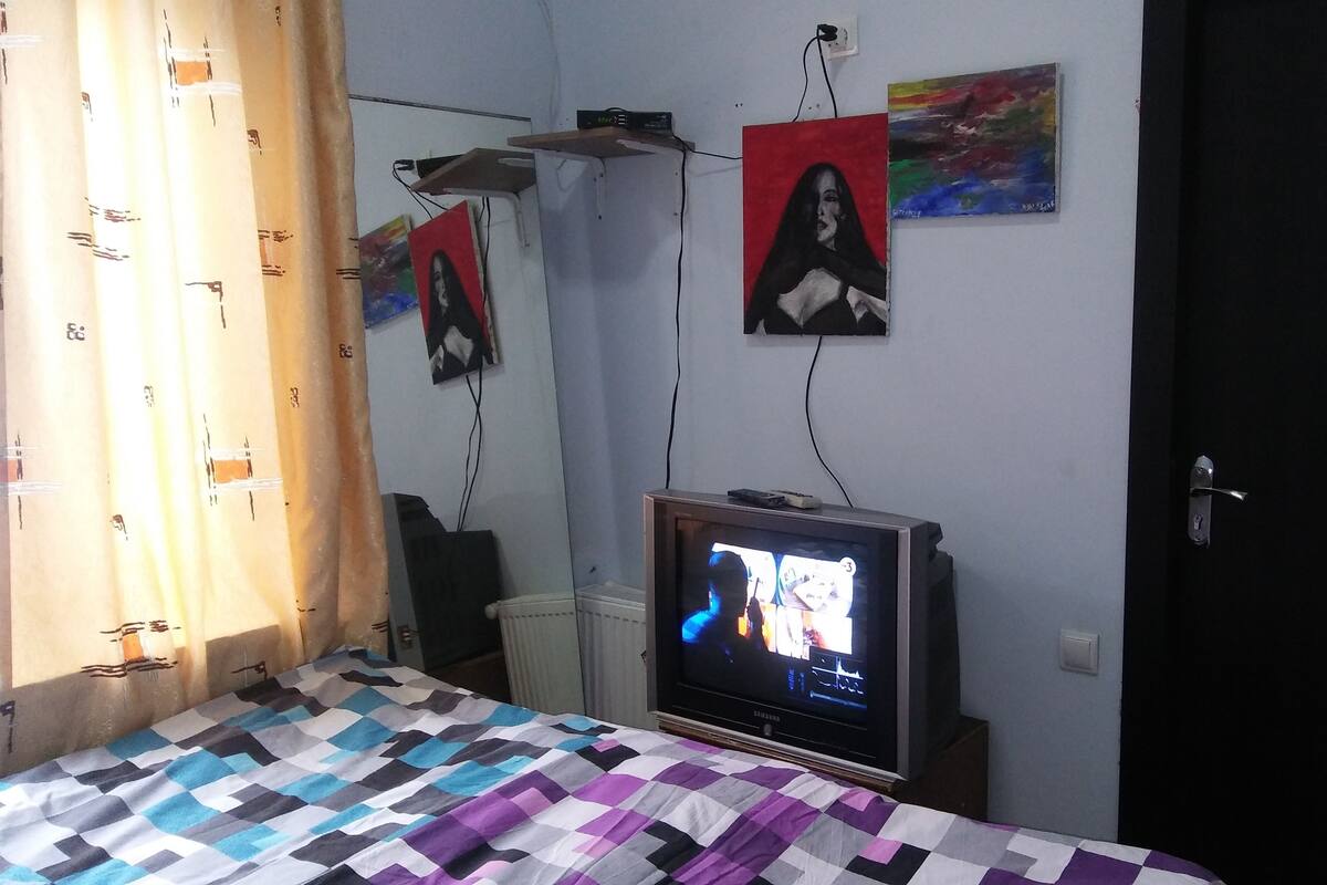 A bedroom with a bed, a television, and wall art.