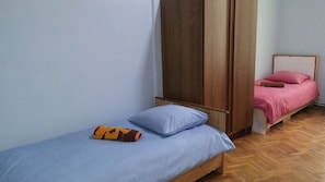 A small, single-bed room with a wooden wardrobe, a blue mattress, and a pink bedspread. - Vareron Hostel (Tbilisi)