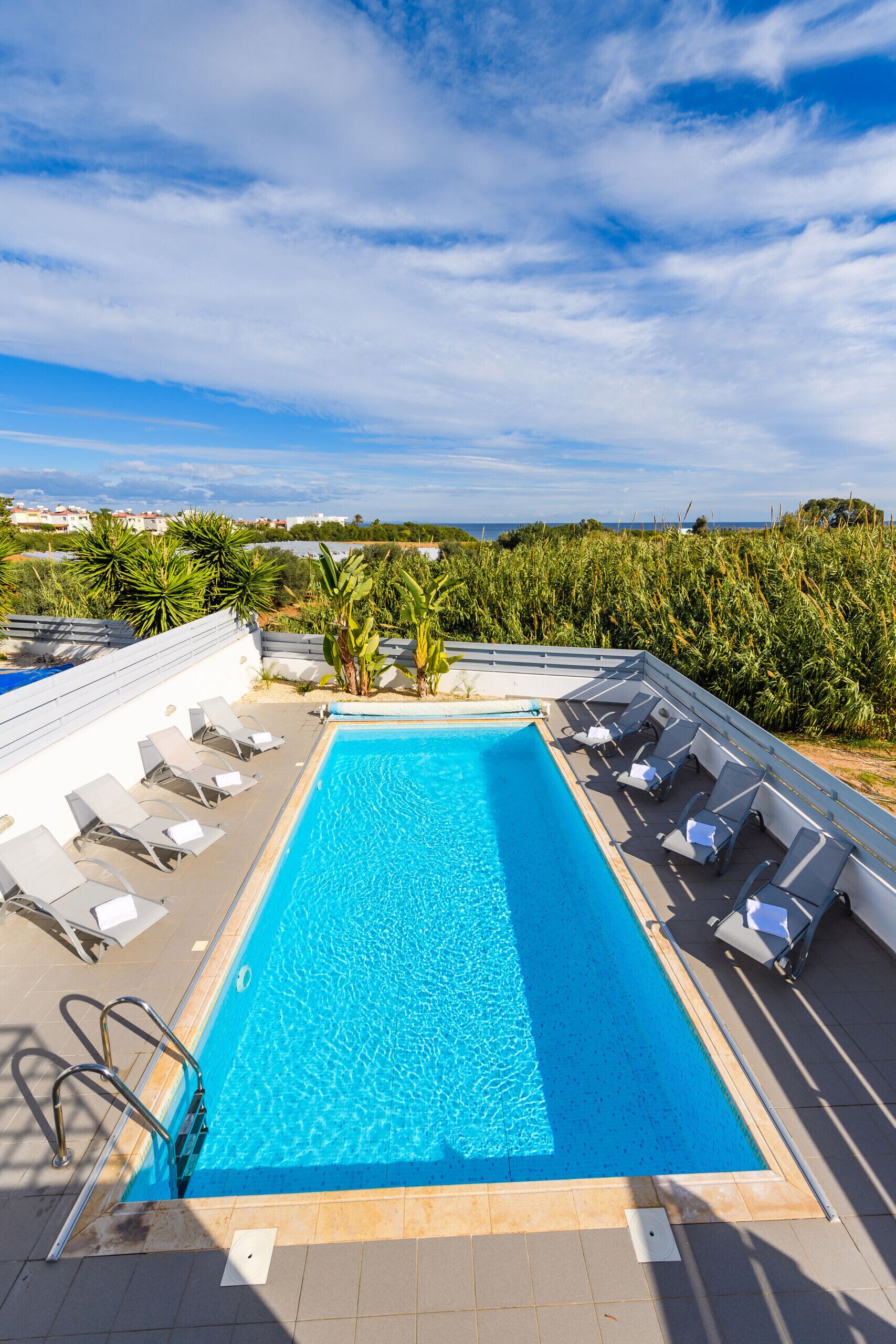 A rectangular pool with clear blue water, surrounded by white lounge chairs and a metal ladder.