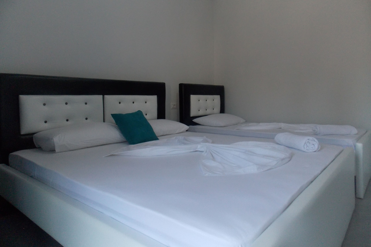 Habitación de hotel con dos camas, cada una con sábanas blancas y una almohada color turquesa.