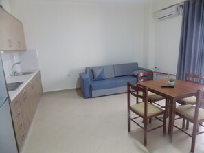 A compact living space with a kitchenette, a sofa, a dining table with chairs, and a small potted plant. - Doka Luxury Apartments (Sarandë)