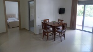 Une pièce comprenant un lit, une table à manger avec des chaises, un téléviseur fixé au mur et une porte-fenêtre coulissante donnant sur un espace extérieur.