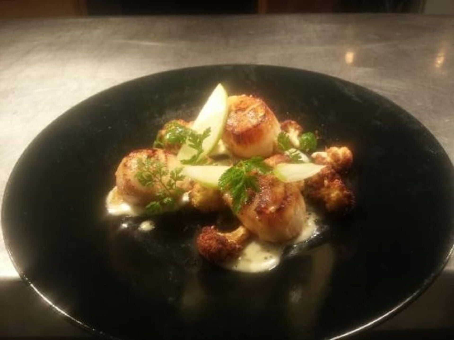 Une assiette de noix de Saint-Jacques poêlées, nappées d’une sauce crémeuse et garnies d’herbes fraîches.