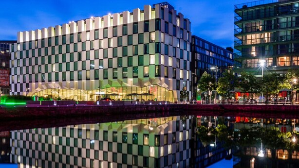 Een modern gebouw met een geruit gevel, een reflectie in het water, en een avondsituatie.
