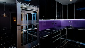Een moderne keuken met roestvrijstalen apparatuur, een paarse accentmuur en een zwart aanrecht.