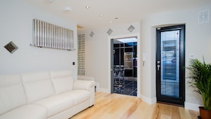 Een moderne woonkamer met een witte bank, een radiator en een deur naar een keuken.