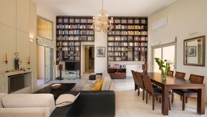 Een ruime woonkamer met een grote boekenkast, een eethoek met een houten tafel en stoelen, en een moderne open haard.