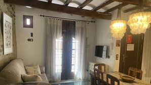 Una sala de estar acogedora con sofá, una mesa de comedor con sillas, televisión y ventana con cortinas.