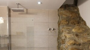 Un baño con pared de piedra, ducha e inodoro.