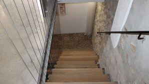 Una escalera de madera con barandales de metal que conduce a un cuarto con pared de piedra y puerta de madera.