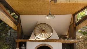 Una zona de cocina al aire libre con chimenea de piedra, bancos de madera y techo de paja.