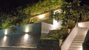 A modern staircase with a stone wall and greenery on the left, leading to a white building with a balcony.