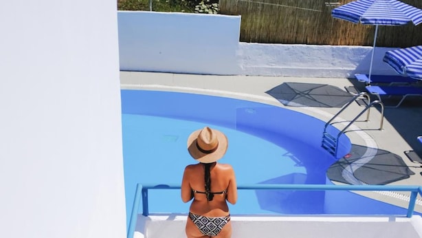 A person descending a marble staircase towards a pool area with lounge chairs and umbrellas. - Kalimera Studios and Apartments (Corfu)