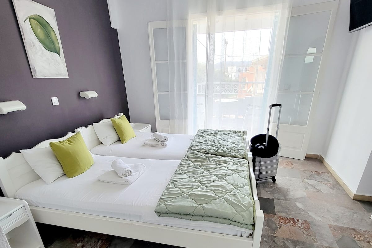 A hotel room with two beds, a large window, a TV, and a suitcase.