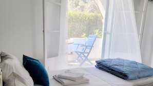 A bedroom with a bed, pillows, a folded towel, and a chair outside. - Kalimera Studios and Apartments (Corfu)