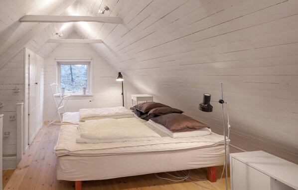 A small, narrow attic bedroom with a sloped ceiling, a window providing natural light, a bedside table with a lamp, and a bed with pillows.