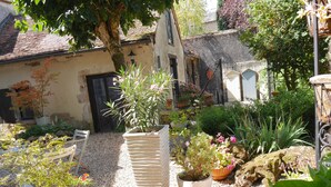A garden with various plants and a cat. There are potted plants, a white bench, and a stone wall. - L'Arbre d'Ange (Montmorillon)