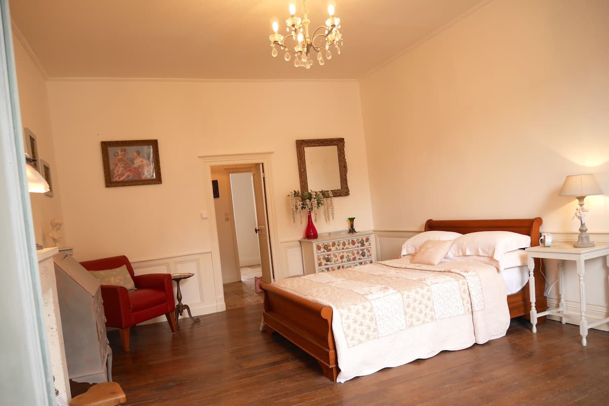 A bedroom with a wooden bed, a red chair, a dresser, and a chandelier.