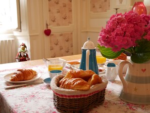 A breakfast setting with croissants, orange juice, and a coffee pot on a floral tablecloth. - L'Arbre d'Ange (Montmorillon)