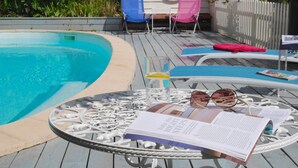 A poolside area with a round table, lounge chairs, and a magazine. - L'Arbre d'Ange (Montmorillon)