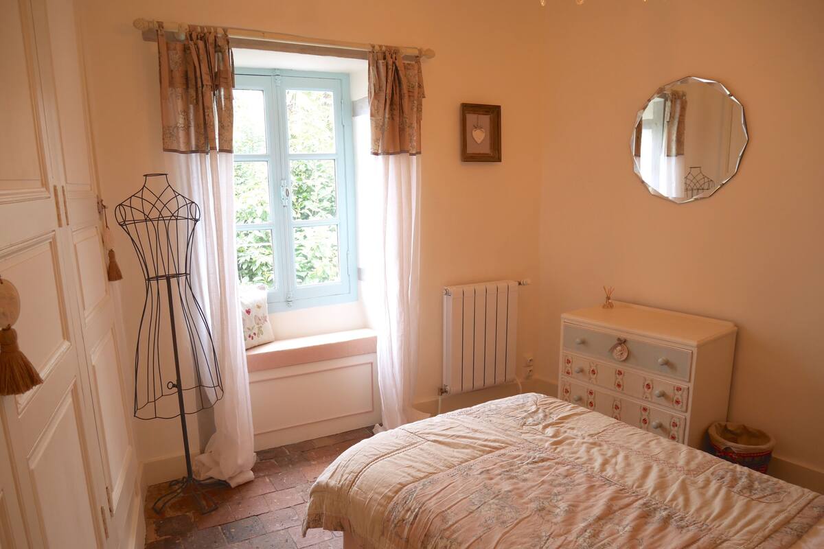 A bedroom with a bed, dresser, window with curtains, radiator, and a mirror on the wall.