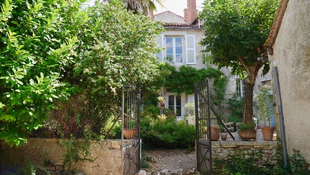 A stone wall with a metal gate leading to a house with a tiled roof and white shutters. - L'Arbre d'Ange (Montmorillon)