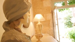 A sculpture of a person wearing a hat, a lamp, and a window with greenery outside. - L'Arbre d'Ange (Montmorillon)