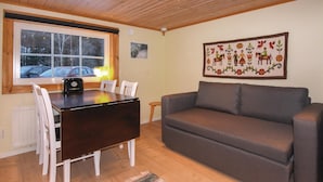 A cozy living room with a wooden ceiling, a gray sofa, a dining table with chairs, and a large window with a view of parked cars outside. - Beautiful home in Ambjörby with sauna (Ambjörby)