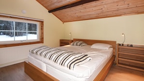 A bedroom with a wooden ceiling, a large window with a view of snow-covered trees, a bed with striped bedding, and bedside tables with lamps. - Beautiful home in Ambjörby with sauna (Ambjörby)