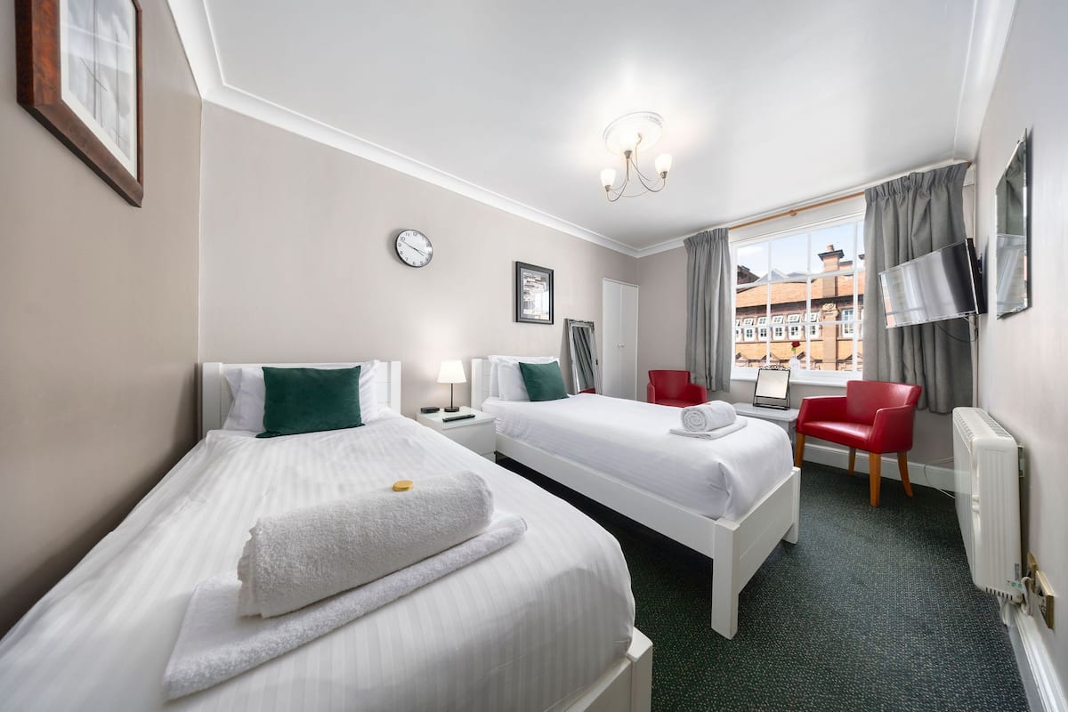A hotel room with two beds, a red chair, a TV, and a window with a view of buildings.