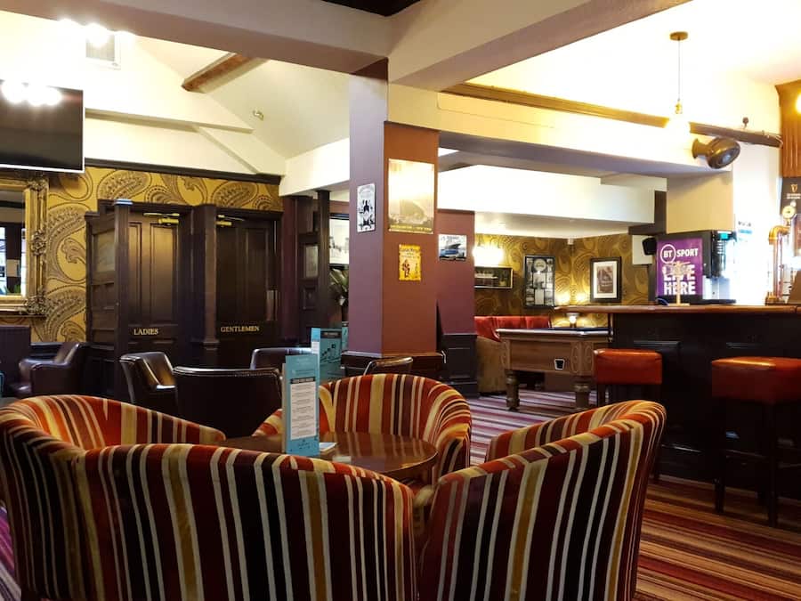 Zona de bar con sillas a rayas, una mesa de billar y una barra con un letrero que dice
