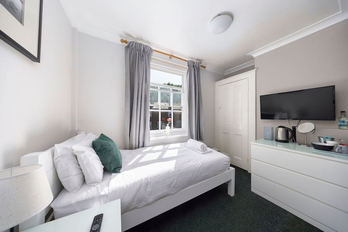 A hotel room with a bed, a TV, a desk, and a window with curtains.