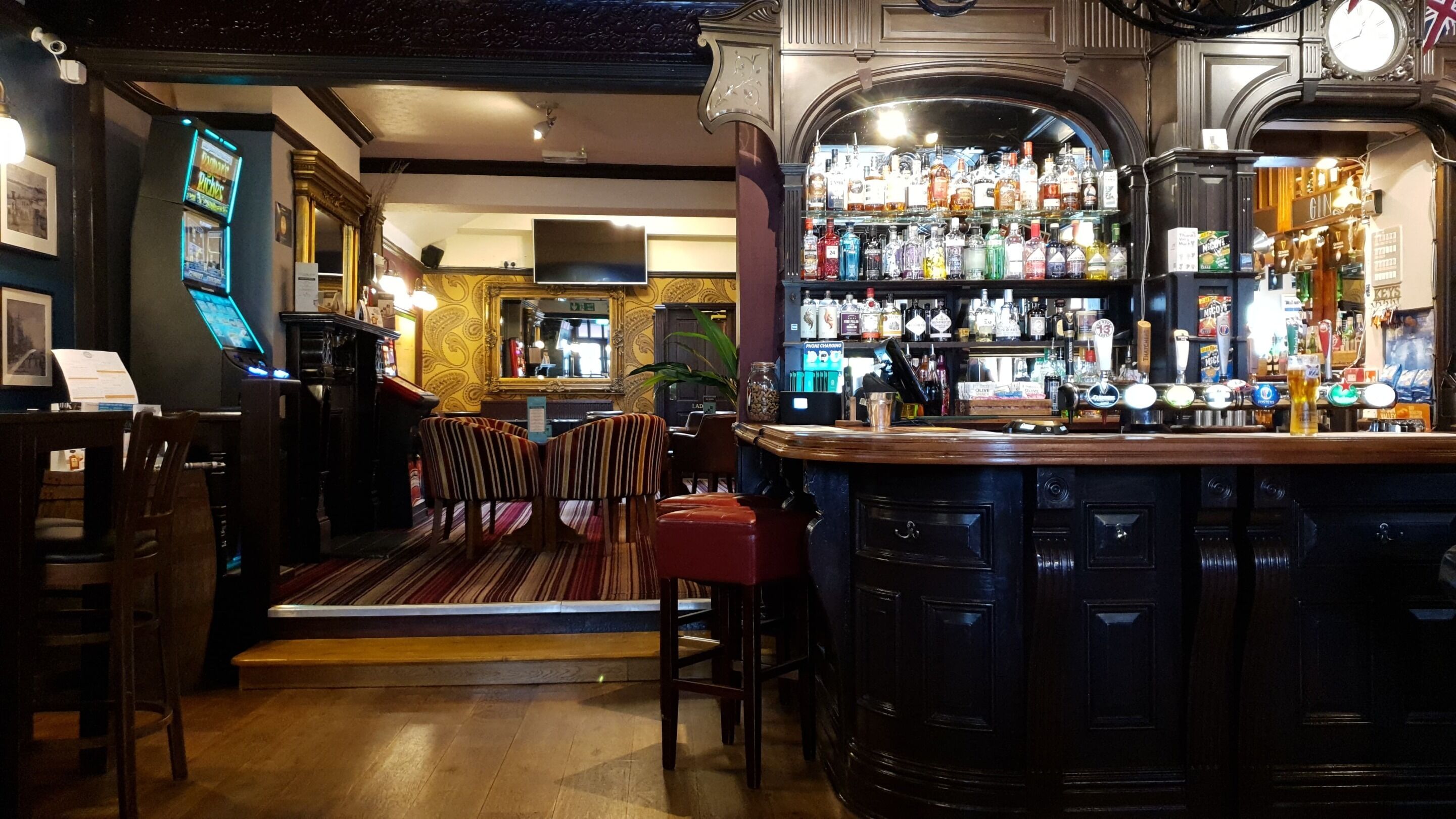 A bar area with a wooden counter, bar stools, and a variety of bottles and glasses.