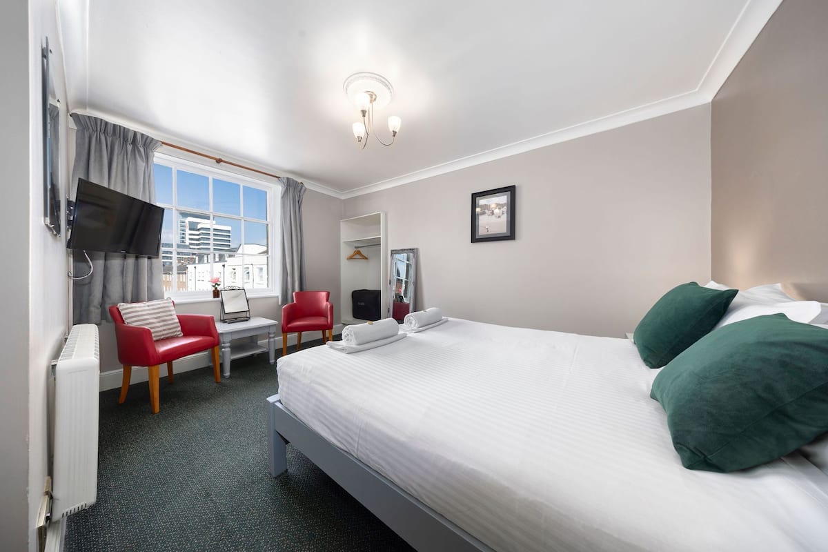 A hotel room with a bed, a desk, a chair, a TV, and a window with curtains.