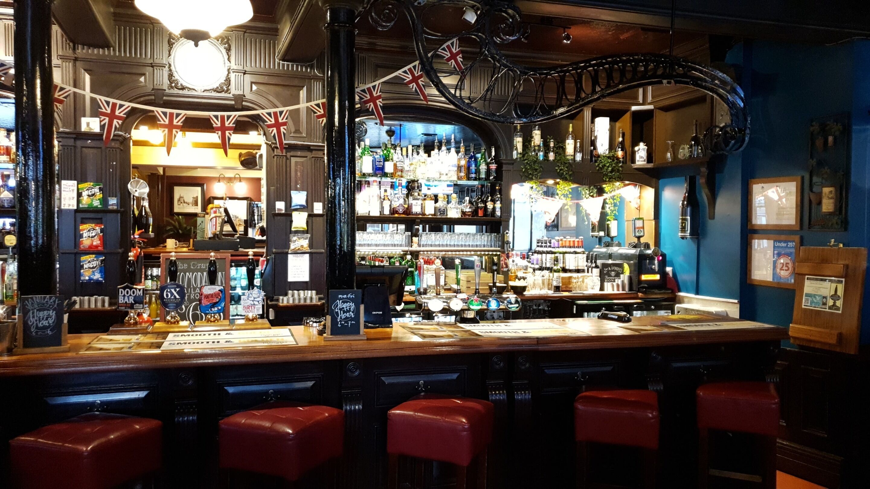 A bar with a variety of liquor bottles, a selection of snacks, and a few stools.