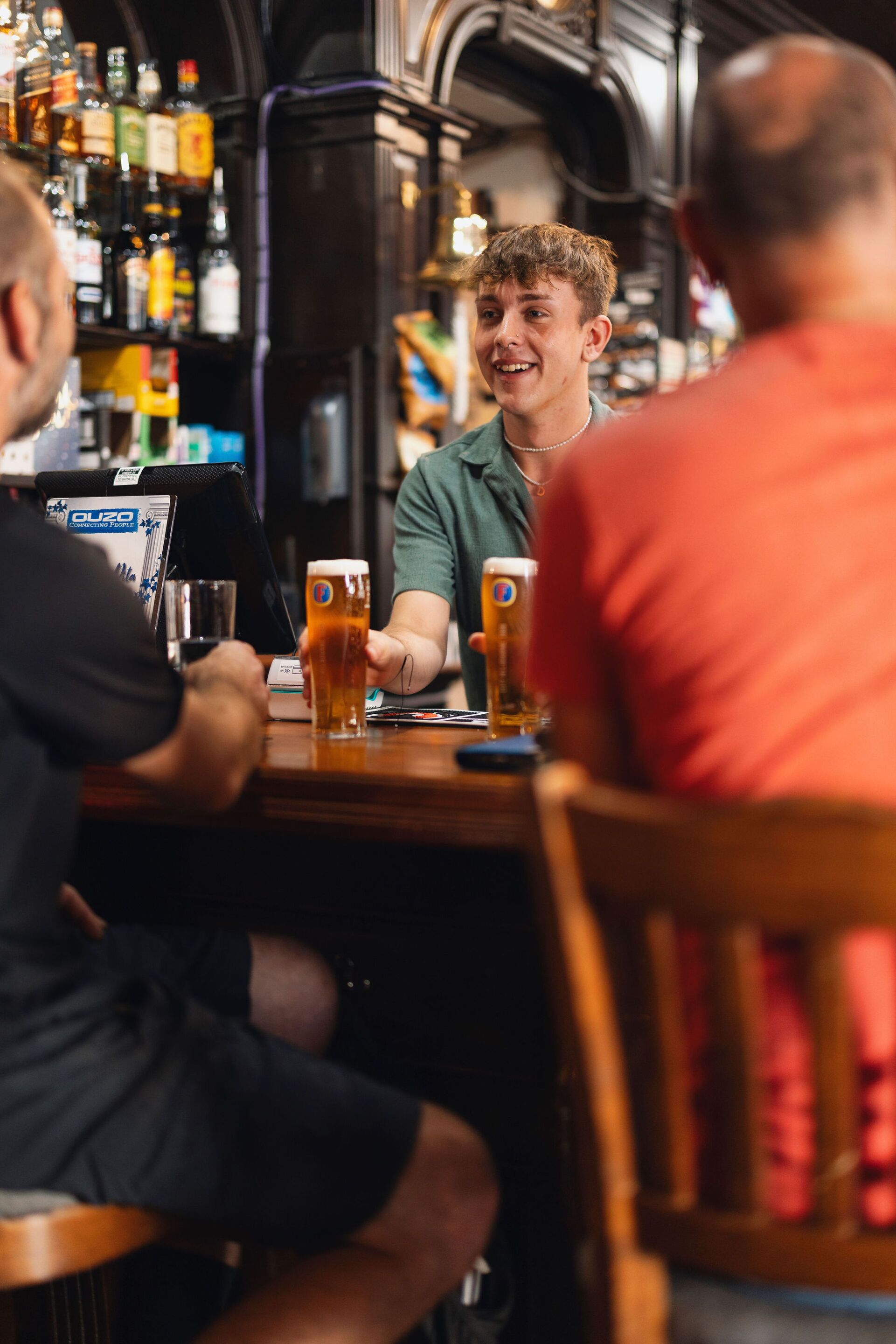 Een bar met een houten toonbank, drankflessen en bierglazen.