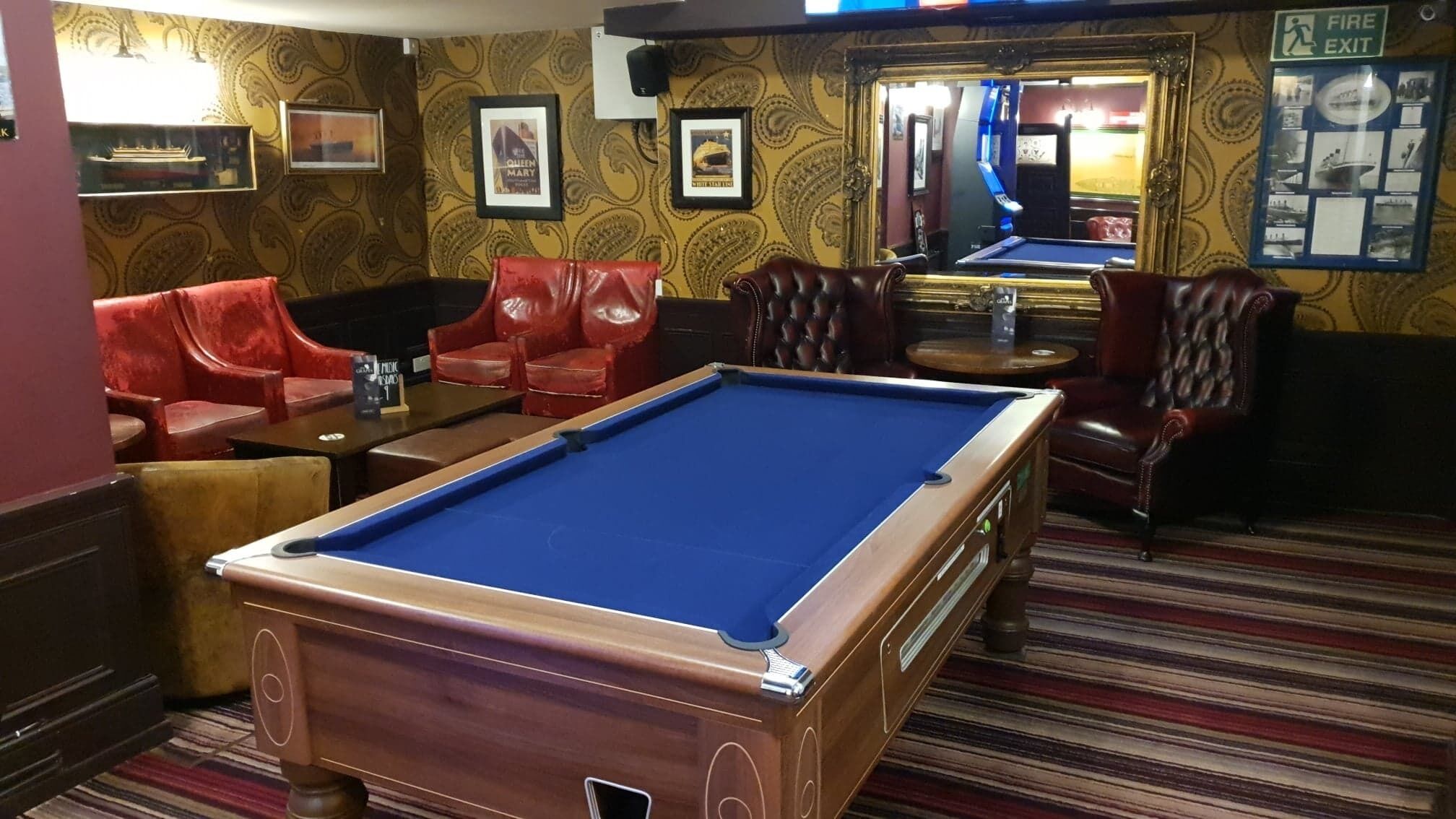 A pool table in a room with red leather chairs and a billiards table.