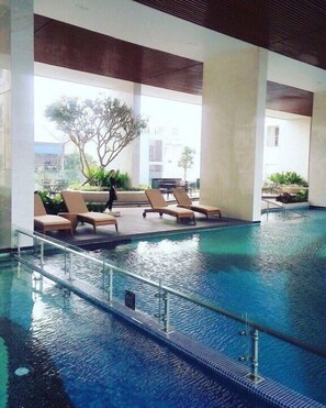 An indoor swimming pool with lounge chairs and a view of buildings outside. - Cozy Botanica Boutique (Ho Chi Minh City)
